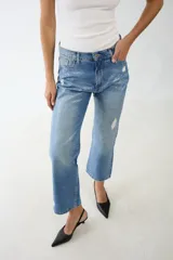 Jean de algodón 100% con lavado azul medio, tiro alto y corte recto/acampanado. Presenta un estampado texturizado tipo cocodrilo en tono más claro y detalles de desgaste/roturas.