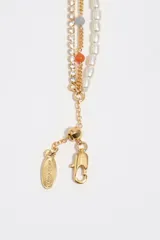 Pulsera dorada multicapa compuesta por una tira de perlas, una cadena fina con pequeños cristales incrustados y cuentas de colores en tonos verdes, naranjas y grises. Presenta un dije en forma de corazón esmaltado en negro y cierre de mosquetón con eslabones de ajuste.