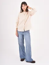 Camisa de manga larga en color crudo, confeccionada en tela con delicado bordado floral en relieve. Presenta cuello redondo con frunces, cierre frontal con botones y mangas abullonadas con puños ajustados.