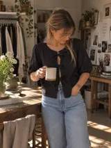 Blusa negra de lino con mangas abullonadas y cierre frontal mediante tres lazos o moños.