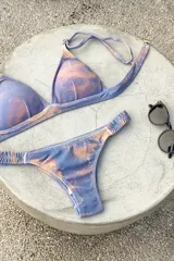 Bikini de dos piezas color marrón, con corpiño triangular fijo con corte bajo el busto, breteles regulables con hebilla y almohadillas desmontables. La bombacha es vedetina con frunce elástico en los costados.