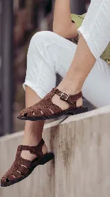 Sandalias tipo cangrejera de cuero color marrón chocolate, con diseño de tiras entrelazadas, suela plana de goma flexible y tira con hebilla metálica ajustable en el tobillo.
