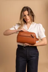 Neceser unisex de símil cuero color marrón coñac, con forma rectangular y asas laterales. Presenta un compartimento principal con cierre superior y un bolsillo frontal con cierre.