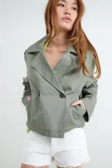 Campera estilo trench corta color beige, con solapas amplias, cierre cruzado de doble botonadura con botones oscuros y diseño holgado.