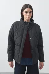 Campera acolchada de nylon color negro, con cuello alto, cierre frontal y botones a presión. Presenta un diseño de rombos y forro interior suave.