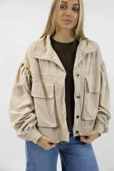 Campera corta de pana color beige, con cuello clásico, cierre frontal con botones y amplios bolsillos con solapa en el pecho. Cuenta con mangas largas abullonadas y diseño holgado.
