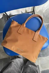 Cartera tipo shopper color negro, de diseño estructurado con doble asa de mano y cierre superior. Presenta sutil grabado de la marca en la parte inferior frontal.