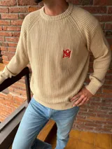 Sweater de punto color beige con cuello redondo, mangas raglán y bordado rojo en el pecho.