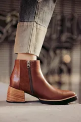 Botín de cuero negro, caña corta, con punta cuadrada y cierre lateral. Presenta un tacón de madera de altura media y detalles en charol con textura de cocodrilo en el talón.