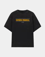 Remera oversize de efecto acid wash en color negro, con diseño gráfico frontal que incluye la leyenda "Nothing Personal" en tono amarillo y detalles de estrellas.
