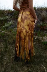 Pollera midi de cuero con estampado marmolado en tonos marrones y mostaza, de corte asimétrico con detalles de largos flecos colgantes en el borde inferior.