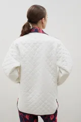 Campera acolchada de corte holgado, color blanco con diseño capitoneado en forma de rombos. Presenta cuello camisero y bordes internos con estampado floral en tonos azul y rojo, cierre frontal con botones a presión y bolsillos laterales.