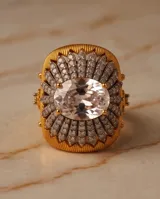Anillo grande de bronce con baño de oro, diseño texturizado en forma de flor con incrustaciones de circón pavé y una piedra central ovalada transparente.