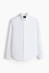 Camisa de vestir blanca con cuello inglés, tapeta clásica y corte ajustado. Presenta mangas largas con puños abotonados y bajo levemente redondeado.