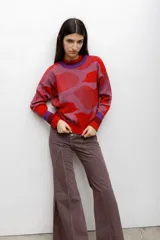 Buzo tejido en técnica jacquard con diseño de formas abstractas en tonos rojos, rosados y violetas. Presenta cuello redondo, mangas largas y puños y ruedo acanalados.