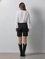 Bermuda de jean color negro, con cierre frontal y botón, bolsillos laterales y diseño clásico de cinco bolsillos.