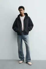 Sudadera tipo hoodie de corte relajado, confeccionada en tejido de algodón con textura estructurada y efecto lavado. Presenta cierre frontal con cremallera, cuello con capucha, manga larga, bolsillos tipo canguro y acabados en rib.