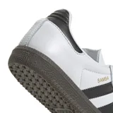 Championes Adidas modelo Samba OG, de diseño clásico con exterior de cuero blanco, tres tiras laterales negras, puntera de gamuza gris y suela de goma color marrón.