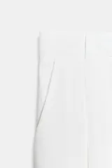 Pantalón negro de tiro alto, con trabillas, bolsillos laterales y de vivo en la espalda. Presenta pliegues en el delantero y cierre frontal con botón.