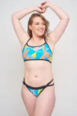 Conjunto de bikini con estampado de hojas de palmera en tonos celeste, amarillo y naranja, con contorno negro. El corpiño es de corte deportivo con tirantes finos y la bombacha es de corte clásico con tiras laterales.
