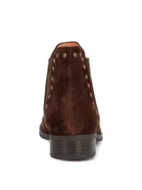 Botines de gamuza color marrón oscuro con diseño tipo chelsea, detalle de tachas metálicas a lo largo del elástico lateral y suela de goma con tacón bajo.