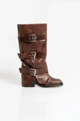 Botas de caña alta confeccionadas en cuero con efecto gastado. Presentan un diseño con tres correas horizontales ajustables mediante hebillas metálicas plateadas. Cuentan con un taco cuadrado bajo y suela de goma.