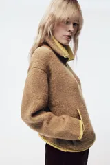 Chaqueta de punto de textura bouclé en color marrón, con cuello subido, manga larga y cierre frontal con cremallera. Presenta detalles de ribetes y acabados en color verde lima a contraste en cuello, cierre, bolsillos y puños.
