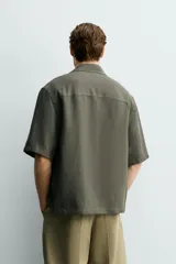 Camisa tipo kimono de corte relaxed fit, color celeste, confeccionada en tejido fluido de viscosa y lino. Presenta cuello con solapas de muesca, manga corta y cierre frontal cruzado con doble botonadura.