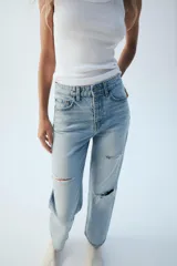 Jeans wide leg de tiro alto y cinco bolsillos, confeccionados en denim con lavado azul medio y efecto desgastado. Presenta cierre frontal con cremallera y botón metálico.