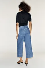 Jeans culotte de tiro alto, color azul, con pernera ancha, nervios marcados en el delantero y bolsillos de parche con botones metálicos. Cuenta con cierre frontal de cremallera y botón metálico.