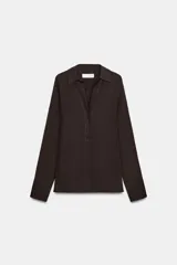Camisa de cuello solapa y escote en pico, con manga larga y cierre frontal mediante botones. Presenta un diseño fluido con bajo asimétrico y aberturas laterales.