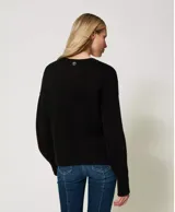 Sweater negro de algodón con cuello redondo, manga larga y corte holgado. Presenta incrustaciones florales decoradas con bordados a mano.