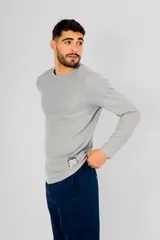 Buzo de manga larga con cuello redondo, confeccionado en tejido de punto con textura tipo waffle. Presenta un diseño minimalista con una pequeña etiqueta decorativa en el ruedo inferior.