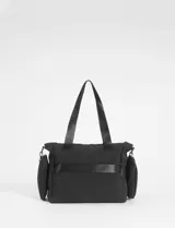 Cartera tipo bolso color beige con detalles en negro, confeccionada en nylon. Presenta múltiples compartimentos externos, incluyendo bolsillos laterales removibles, cierre superior y correas de hombro resistentes.