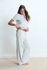 Pijama de dos piezas compuesto por una remera de manga corta y un pantalón largo, confeccionado en tejido de algodón gris claro con estampado de pequeños corazones negros.