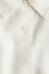 Camisa de viscosa color marfil, de corte holgado con hombros caidos, mangas cortas hasta el codo, cuello camisero y botonadura frontal. Incluye un cinturon fino extraible para ajustar en la cintura y aberturas laterales en el bajo.