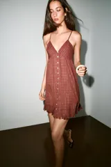 Vestido mini marrón terracota con finas rayas verticales de hilo metalizado, escote en V, tirantes finos ajustables, cierre frontal con botones y detalle de volados desflecados en el borde inferior.