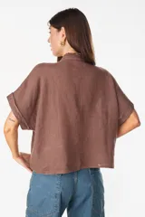 Camisa de lino marrón con mangas cortas, cuello mao con volados, cierre frontal con botones blancos y detalles de calados verticales en el frente.