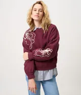 Saco de algodón color bordó con bordado floral en cuerda de color crudo en el frente y las mangas, cuello redondo acanalado, mangas largas y puños ajustados.