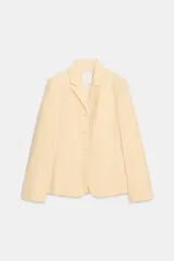 Blazer de popelina de algodón color amarillo pastel, con cuello de solapa, manga larga y cierre frontal de tres botones. Cuenta con bolsillos de plastrón en el delantero.