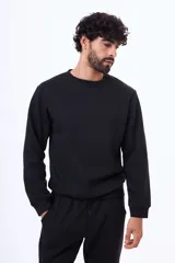 Buzo de felpa color negro, con cuello redondo, mangas largas y puños elásticos.