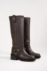 Botas de cuero color marrón oscuro, de caña alta, con taco cuadrado y correa con hebilla metálica alrededor del tobillo.