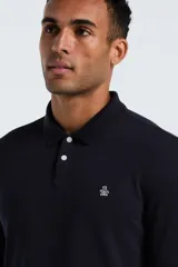 Polo de manga larga color negro, confeccionada en tejido otoman, con cuello clásico y cierre frontal de dos botones. Presenta el logo de la marca bordado en el pecho.