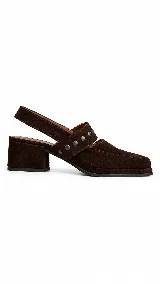 Zapatos destalonados de gamuza marrón con taco cuadrado medio y punta cuadrada. Tienen una tira en el empeine decorada con tachas metálicas redondas y tira elástica trasera.