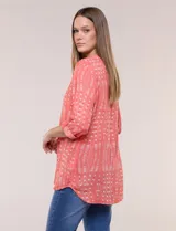 Blusa turquesa de silueta suelta confeccionada en tejido liviano, con escote en V, pequeña cartera frontal con botones decorativos y mangas 3/4 con presilla para arremangar. Presenta patrón estampado geométrico tipo tie-dye y ruedo curvo.