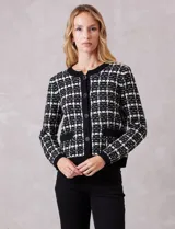 Cardigan de tejido de punto con diseño cuadrillé en contraste blanco y negro. Presenta escote redondo, cierre frontal con botones metálicos y dos bolsillos delanteros. Posee terminaciones en rib en cuello, puños, cartera y ruedo.