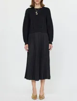 Conjunto compuesto por un buzo de tejido calado con cuello redondo y mangas largas, y un vestido midi de satén con falda plisada. Ambas piezas son de color negro y pueden combinarse o utilizarse por separado.