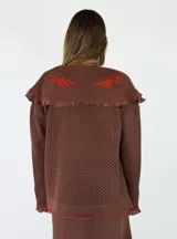 Saco tejido de punto color azul con diseño calado, cuello grande con bordados florales en tono crudo, volados decorativos y cierre frontal con un botón.