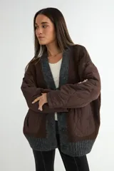 Saco tipo cardigan de punto gris con diseño híbrido. Presenta mangas largas y bolsillos frontales de tela técnica acolchada en color negro, con cierre frontal de botones y bordes acanalados.