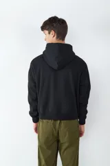 Buzo con capucha de color negro, con bolsillo tipo canguro frontal, mangas largas con puños elásticos y cordones ajustables en el cuello.
